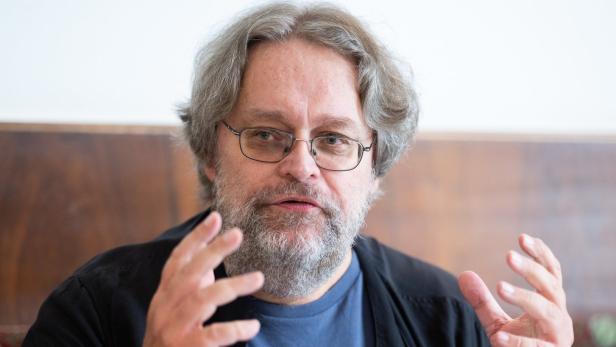 Ein Mann mit Brille und grauem Haar gestikuliert mit seinen Händen.