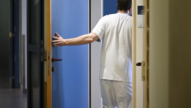 Ein Mann in weißer Kleidung öffnet eine blaue Tür in einem Flur.