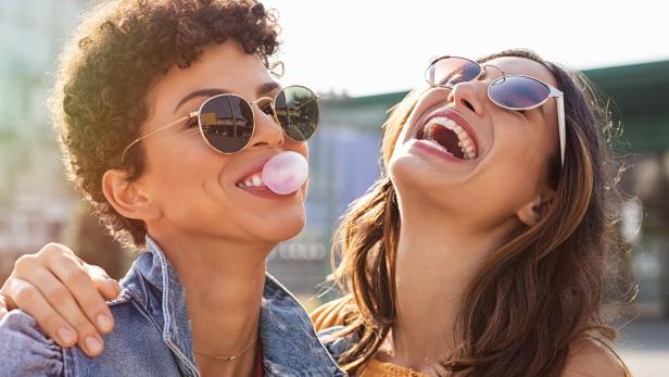 Zwei junge Frauen lachen und eine von ihnen macht eine Kaugummiblase.