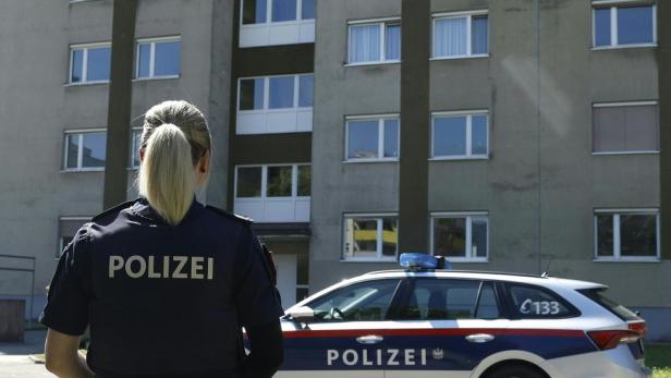 Eine Polizistin steht vor einem Mehrfamilienhaus und einem Polizeiauto.