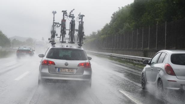 Ein silberner VW fährt mit Fahrrädern auf dem Dach bei Regen auf der Autobahn.