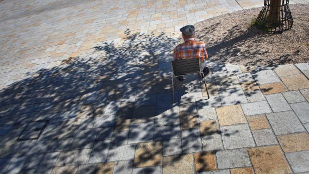 Ein Mann sitzt auf einer Bank im Schatten eines Baumes.