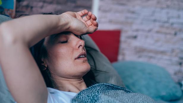 Frau liegt mit Erkältung und hohem Fieber im Bett