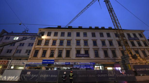 Zwei Bauarbeiter stehen vor einem Gebäude, an dem Bauarbeiten stattfinden.