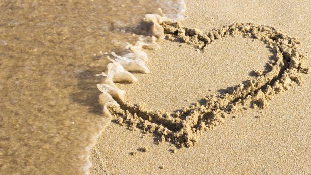 Eine Welle umspült ein in den Sand gezeichnetes Herz.