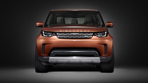 Ein orangefarbener Land Rover Discovery, frontal aufgenommen, vor einem dunklen Hintergrund.