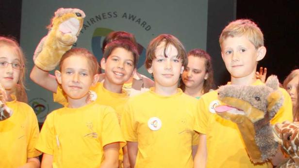 Eine Gruppe von Kindern mit gelben T-Shirts und Handpuppen auf einer Bühne.