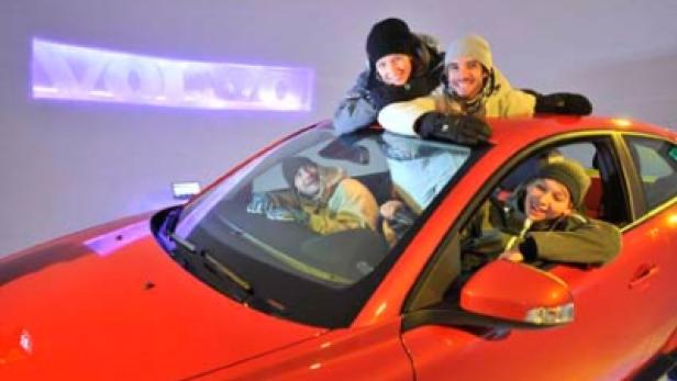 Vier Personen posieren auf und in einem roten Auto.