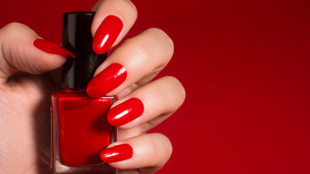 Eine Hand hält eine Flasche roten Nagellack vor einem roten Hintergrund.