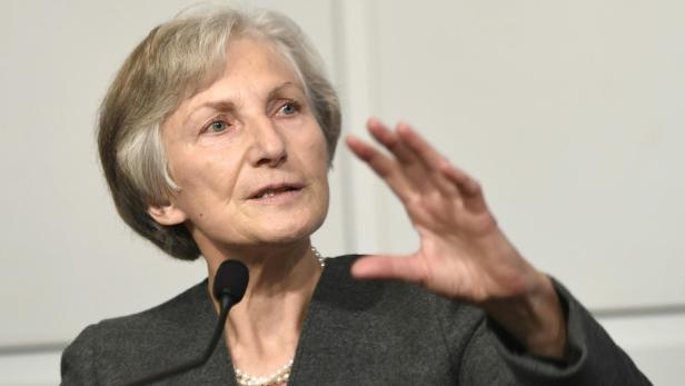 Eine Frau mit kurzem, grauem Haar spricht vor einem Mikrofon und gestikuliert mit der Hand.