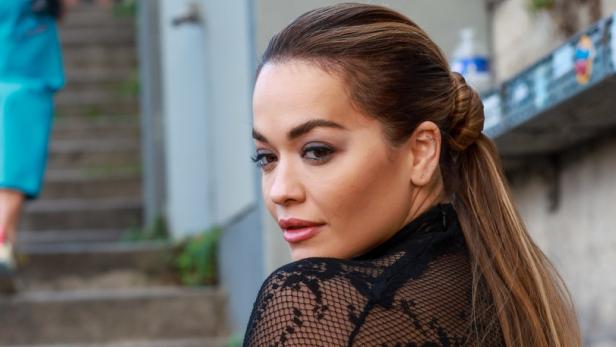 Rita Ora trägt ein schwarzes Spitzenoberteil und blickt über ihre Schulter.