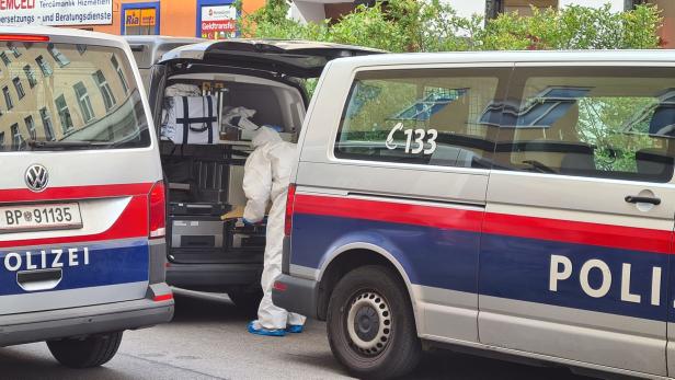 Ein Mitarbeiter der Spurensicherung in Schutzanzug arbeitet an einem Einsatzort neben Polizeifahrzeugen.