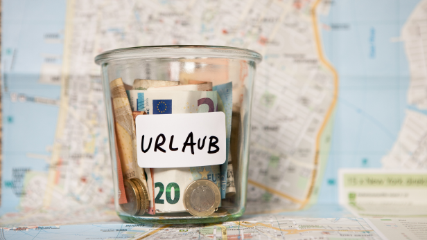 Ein Glas mit Geld und dem Wort „Urlaub“ steht auf einer Landkarte.