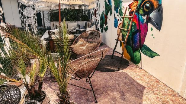 Ein Außenbereich mit Korbstühlen, Sonnenschirm und einem Wandgemälde eines bunten Papageis.