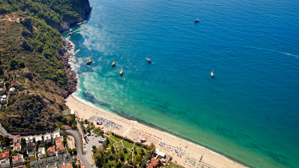 Luftaufnahme eines Strandes mit türkisfarbenem Wasser und mehreren Booten.