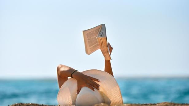 Young woman reads a book on the beach stock photo