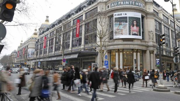 Menschen überqueren eine Straße vor dem Kaufhaus Printemps in Paris.