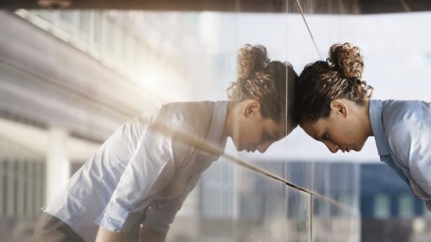 Frau steht mit dem Kopf an einer Glasscheibe.