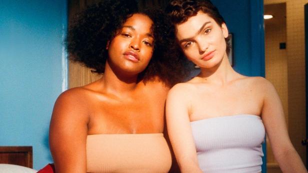 Zwei Frauen sitzen auf einem Bett mit einem rosa Fellteppich.