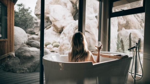 Eine Frau entspannt mit einem Getränk in der Badewanne mit Blick auf Felsen.