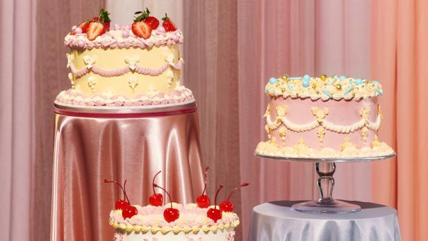 Drei verzierte Kuchen stehen auf Tischen mit pastellfarbenen Tischdecken.