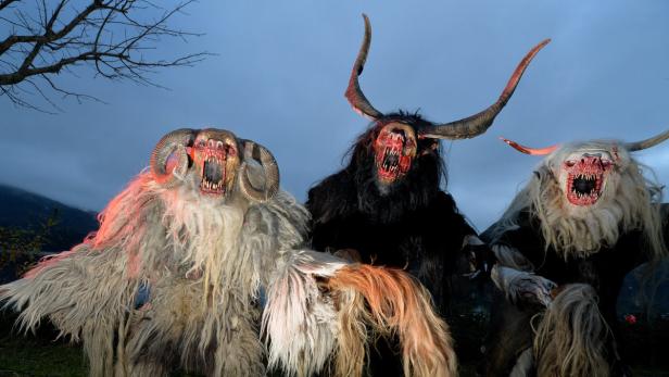 Drei furchterregende Krampus-Gestalten mit Hörnern und Fellkostümen stehen im Dunkeln.