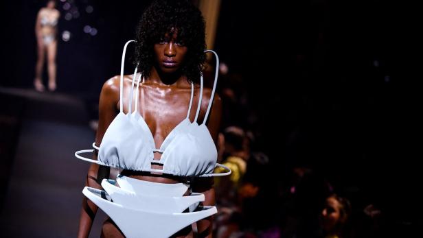 Eine Frau präsentiert ein futuristisches, weißes Bikini-Ensemble auf dem Laufsteg.