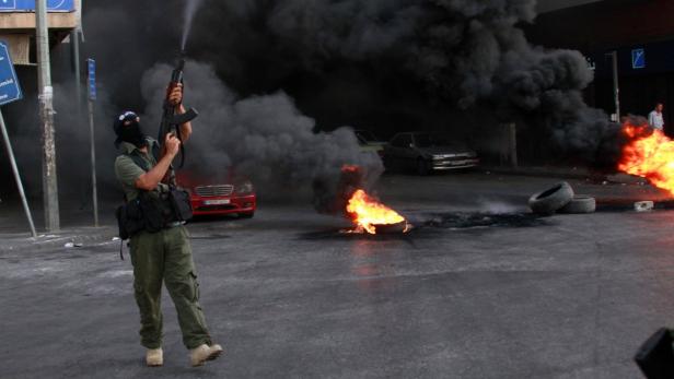 A Sunni Muslim gunman, wearing a mask, fires his weapon in front of burning tires, in solidarity with Salafist leader Ahmad al-Assir in Tripoli, northern Lebanon, June 23, 2013. At least three Lebanese soldiers were killed in the coastal city of Sidon on Sunday in clashes with followers of a Sunni Islamist cleric who is a fierce critic of Hezbollah&#039;s military intervention in neighbouring Syria, a security official said. Sources in the city said the fighting broke out when a follower of Sheikh Ahmed al-Assir was arrested at an army roadblock in Sidon, 40 km (28 miles) south of Beirut. REUTERS/Omar Ibrahim (LEBANON - Tags: POLITICS CIVIL UNREST TPX IMAGES OF THE DAY)