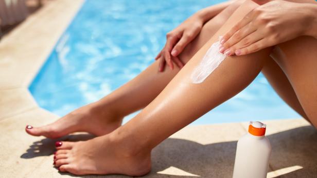 Eine Frau cremt ihre Beine am Pool mit Sonnencreme ein.