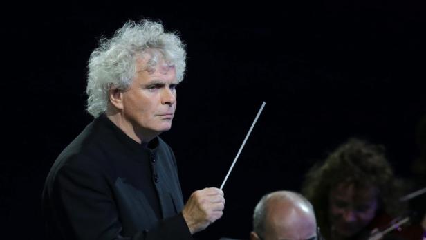 Ein Dirigent mit weißem, lockigem Haar dirigiert ein Orchester.