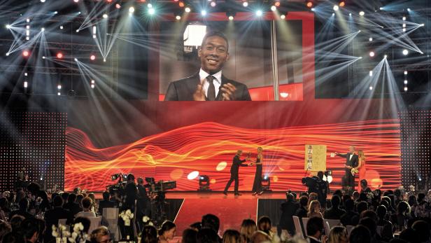 Eine Preisverleihung mit Publikum und einer Live-Übertragung eines Mannes im Anzug.