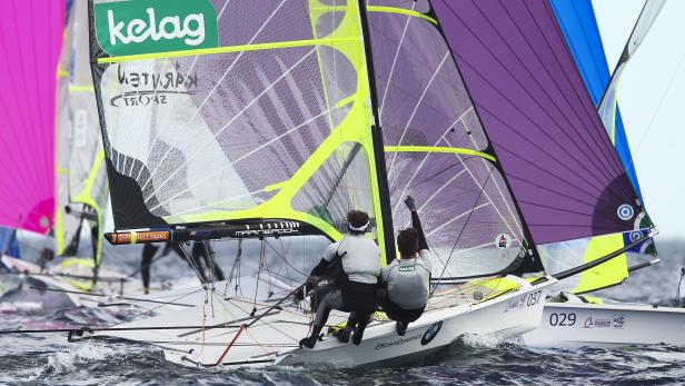 Zwei Segler steuern ein Boot mit „kelag“- und „EfficientDynamics“-Logos bei einer Regatta.