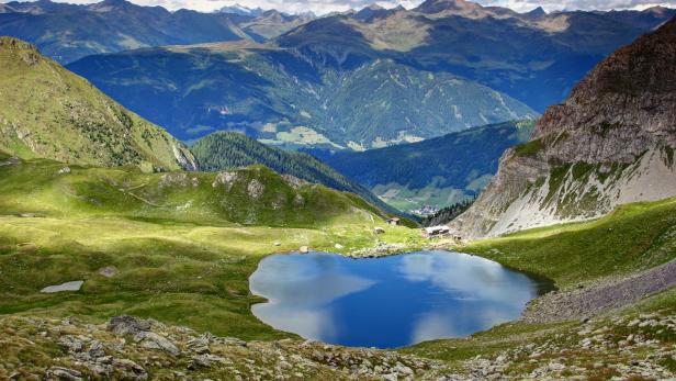 Ein Bergsee spiegelt den Himmel und die umliegende grüne Landschaft wider.