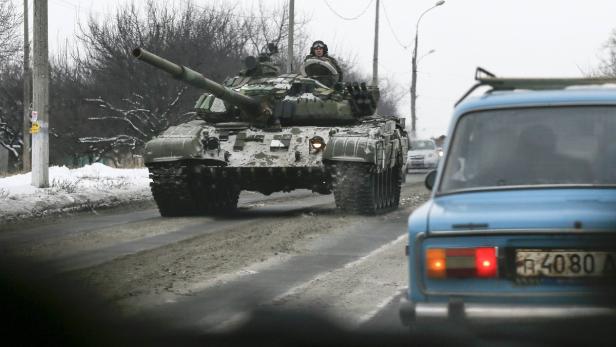 Ein Panzer fährt auf einer verschneiten Straße an einem blauen Auto vorbei.