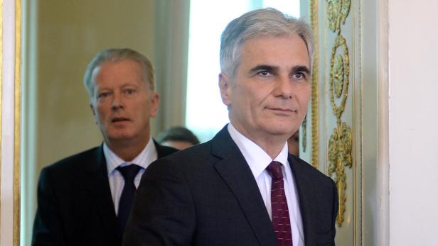 Zwei Männer in Anzügen stehen in einem Raum mit verzierten Wänden.