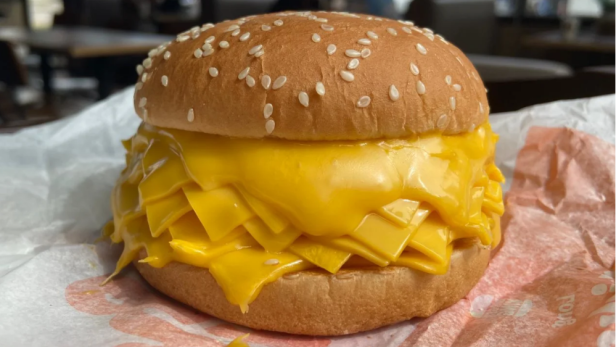 Ein Cheeseburger mit sehr viel Käse liegt auf einem Papier.