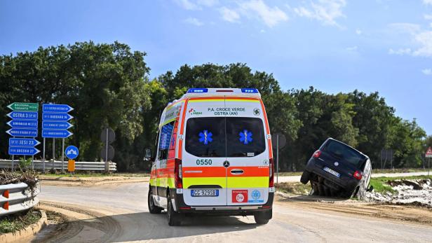 Ein Krankenwagen fährt an einem verunglückten Auto vorbei, vermutlich nach einer Überschwemmung in Italien.