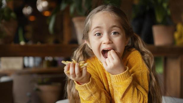 Ein Mädchen isst Pommes Frites mit großem Appetit.