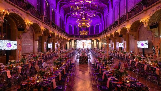Ein festlich dekorierter Saal mit langen Tischen und violetter Beleuchtung für eine Veranstaltung.