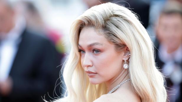 Gigi Hadid mit blonden, gewellten Haaren und auffälligem Schmuck auf einem roten Teppich.