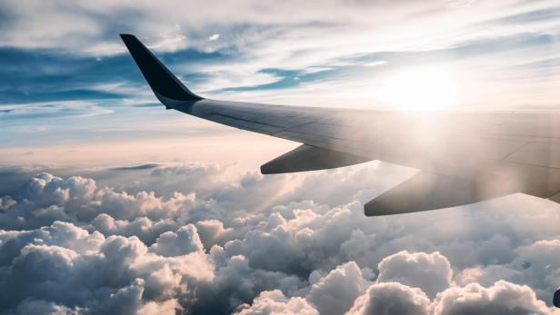 Blick aus einem Flugzeugfenster auf eine Wolkendecke bei Sonnenaufgang.