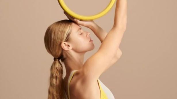 Eine Frau balanciert einen gelben Yogaring auf ihrem Kopf.