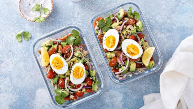 Zwei Salatschüsseln mit Avocado, Tomaten, Eiern und Zitrone stehen auf einem Tisch.