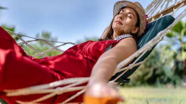 Eine Frau entspannt mit einem Getränk in einer Hängematte.