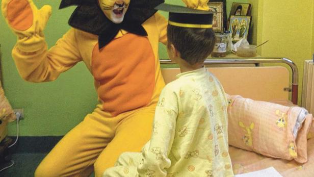 Eine Person im Löwenkostüm unterhält ein Kind in einem Krankenzimmer.