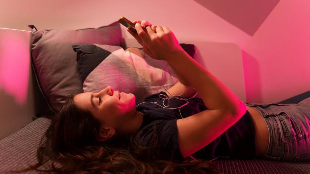 Symbolbild: Eine Frau liegt auf dem Bett und benutzt ihr Smartphone.