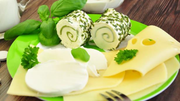 Käseröllchen mit Kräutern, Mozzarella und Käsescheiben auf einem Teller.