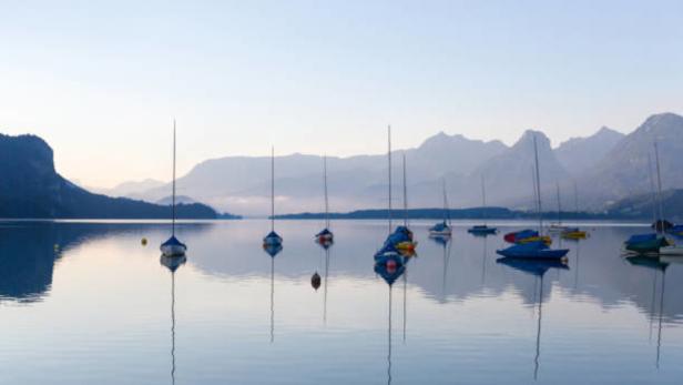 Mehrere Segelboote liegen auf einem ruhigen See vor einer Bergkulisse.