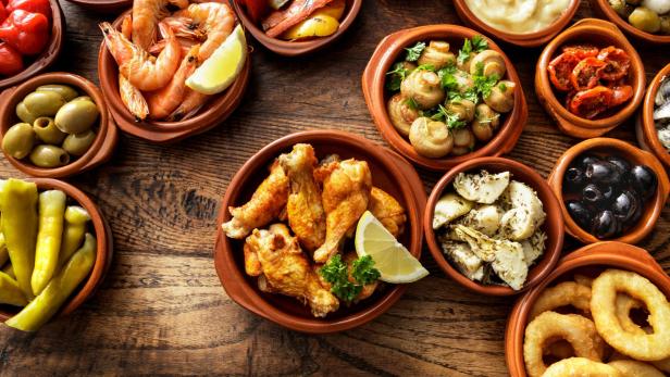 Verschiedene Tapas-Gerichte in kleinen Schalen auf einem Holztisch.