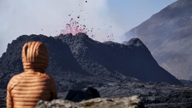 Eine Person in orangefarbener Jacke beobachtet einen Vulkanausbruch.